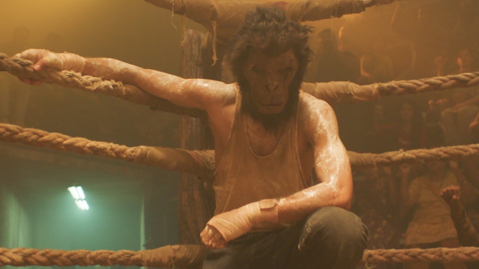 A man in a monkey mask (Dev Patel) rests in the corner of a boxing ring in Monkey Man (2024).